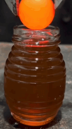 An Orange Ball Is Being Held Over A Jar Of Liquid GIF