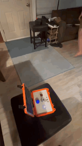 an orange case with a tablet inside of it sits on a black ottoman in a living room