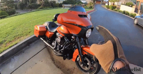 An Orange Harley Davidson Motorcycle Is Parked On The Side Of A Road GIF