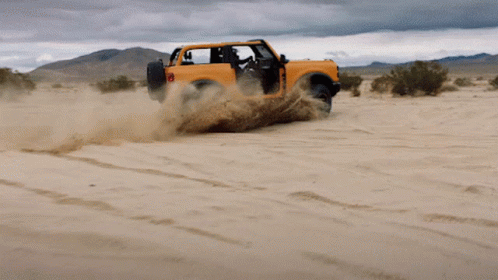 An Orange Jeep Is Driving Through A Sandy Area GIF
