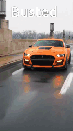 An Orange Mustang Is Driving Down A Street With The Word Busted On The Bottom GIF