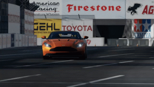 An Orange Sports Car Is Driving Down A Road In Front Of A Sign That Says Toyota GIF