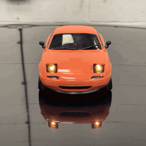 An Orange Toy Car Is Sitting On A Black Table GIF