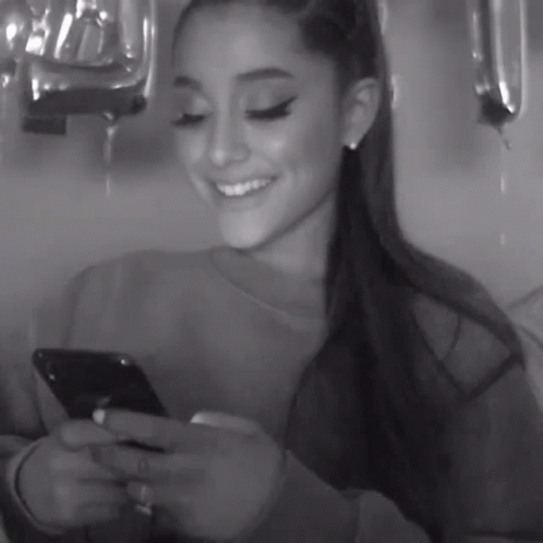 Ariana Grande Is Smiling While Looking At Her Phone GIF