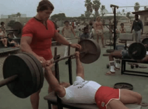 Arnold Schwarzenegger Helping Man Lift Barbell On Bench GIF