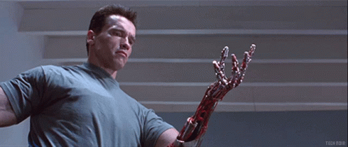 Arnold Schwarzenegger Is Holding A Bloody Robotic Arm In A Scene From Terminator GIF