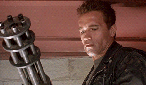 Arnold Schwarzenegger Is Holding A Machine Gun In His Hand GIF