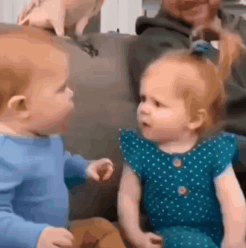 Baby and Little Girl Sitting on Couch Looking at Each Other