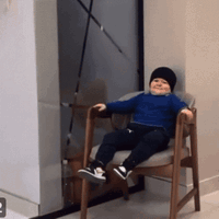 Baby Sitting In Chair Wearing Black Hat GIF