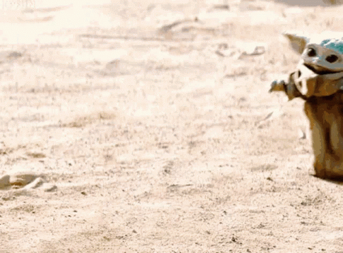 Baby Yoda Sitting On Sandy Beach Next To Person GIF