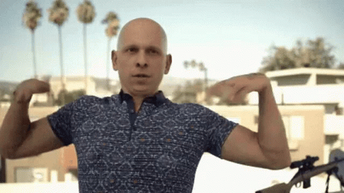 Bald Man in Blue Shirt Flexing Muscles Holding Gun