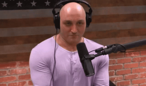 Bald Man in Headphones at Microphone With American Flag