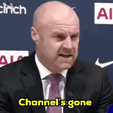 Bald Man in Suit and Tie at Mic