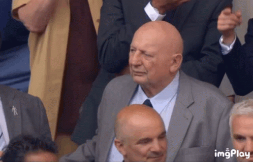 Bald Man In Suit And Tie Sitting In Crowd GIF