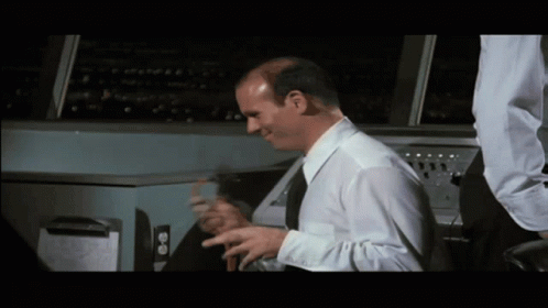 Bald Man in White Shirt and Black Tie Sitting at Machine