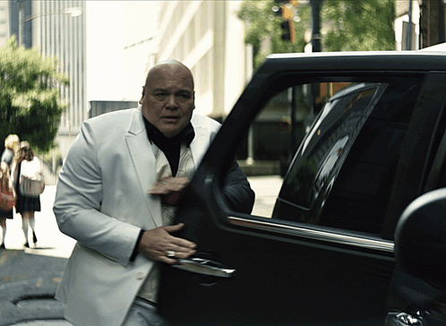 Bald Man in White Suit Exiting Black Car