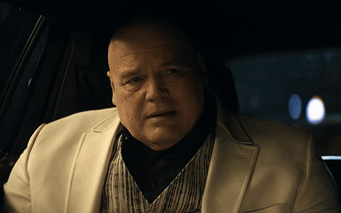 Bald Man in White Suit Sitting in Car
