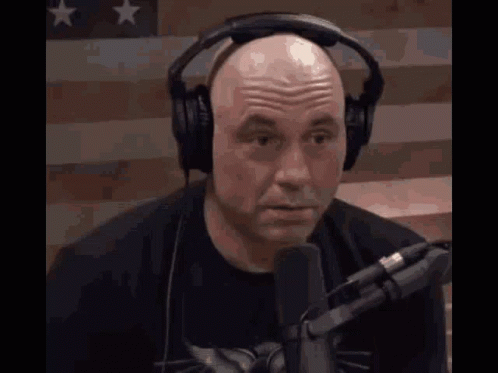 Bald Man Talking Into Microphone Near American Flag