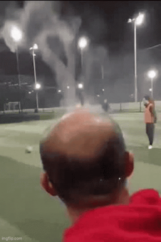 Bald Man Watching Fireworks On Soccer Field At Night GIF