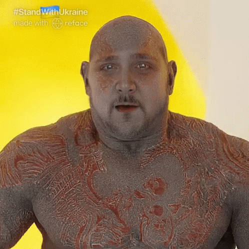 Bald Man With Beard And Chest Tattoos In Front Of Yellow Wall GIF