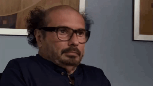Bald Man With Beard And Glasses Sitting In Front Of Picture GIF