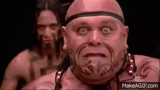 Bald Man With Face Tattoo In Front Of Another Bald Man GIF