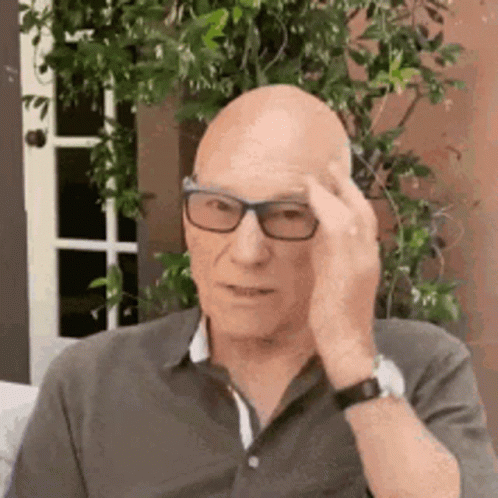 Bald Man With Glasses On Couch Hand On Forehead GIF