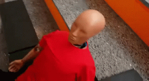 Bald Mannequin In Red Shirt On Concrete Floor GIF