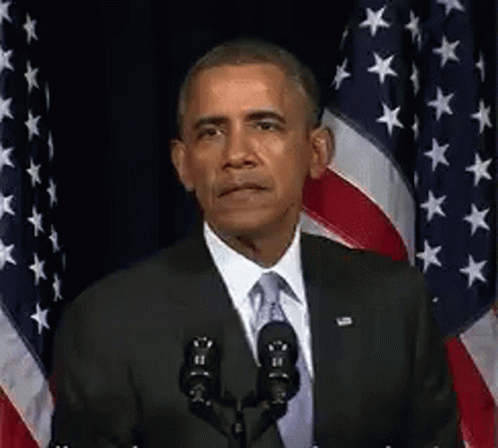 Barack Obama Is Giving A Speech In Front Of A Microphone In Front Of American Flags . GIF