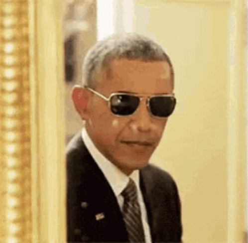 Barack Obama Is Wearing Sunglasses And A Suit And Tie While Peeking Out Of A Picture Frame . GIF
