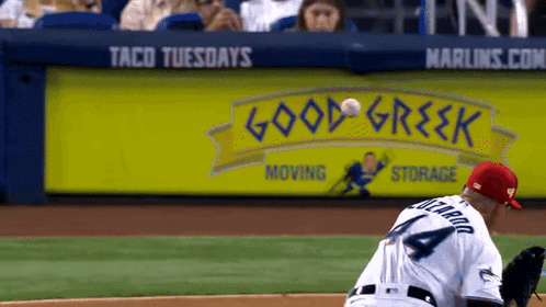 Baseball Player Throws Ball in Front of Good Greek Sign