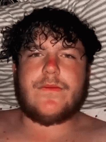 Bearded Curly-Haired Man Laying in Bed With Red Nose