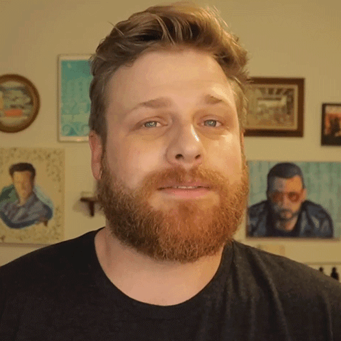Bearded Man In Black Shirt In Front Of Paintings GIF