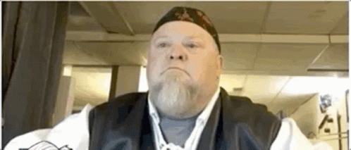 Bearded Man in Hat and Vest Looks at Camera