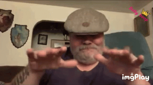 Bearded Man in Hat Sitting with Outstretched Hands