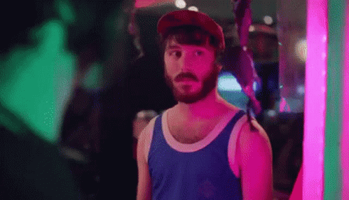 Bearded Man in Tank Top and Hat in Front of Neon Sign