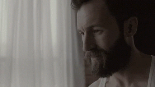 Bearded Man in White Tank Top Looking Out Window