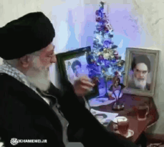 Bearded Man Looking At Picture Near Christmas Tree GIF