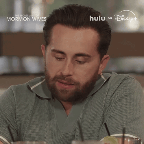 Bearded Man Sitting at Table in Front of Hulu on Disney+ Sign