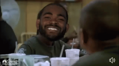 Bearded Man Smiling at Another at Table With Drinks
