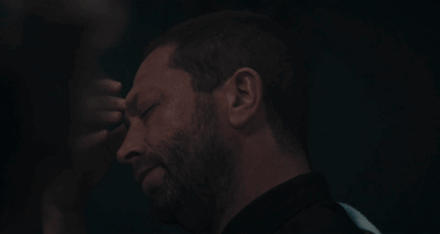 Bearded Man Touching Forehead In Dark Room GIF