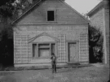 Black and White Man in Front of Small Wooden House