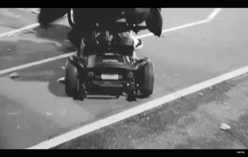 Black and White Person Driving Lawn Mower Down Street