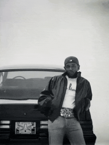 Black and White Photo of Man Standing in Front of Car With License Plate Saying X