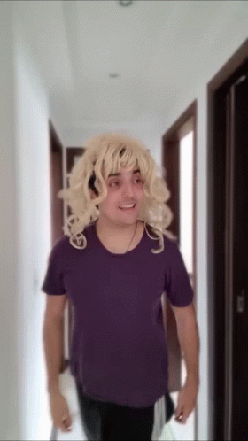 Blonde Wig Man in Purple Shirt Walking Down Hallway