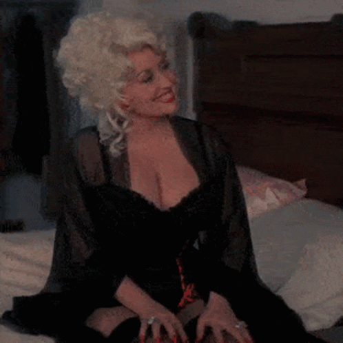 Blonde Woman in Black Dress Sitting on Bed