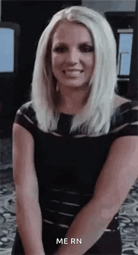 Blonde Woman in Black Dress Smiling With Hands Behind Back