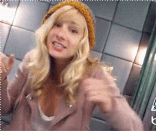 Blonde Woman In Pink Jacket And Yellow Beanie Pointing GIF