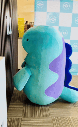 Blue and Purple Stuffed Animal Sitting in Front of Checkered Wall