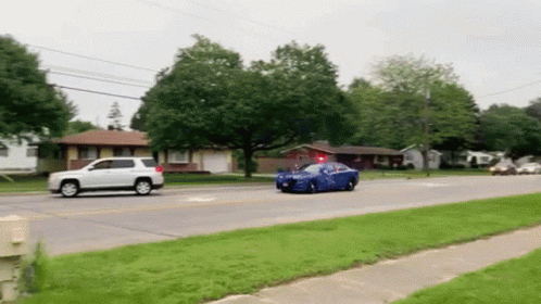 Blue Car Driving Down Street Next to White SUV and House